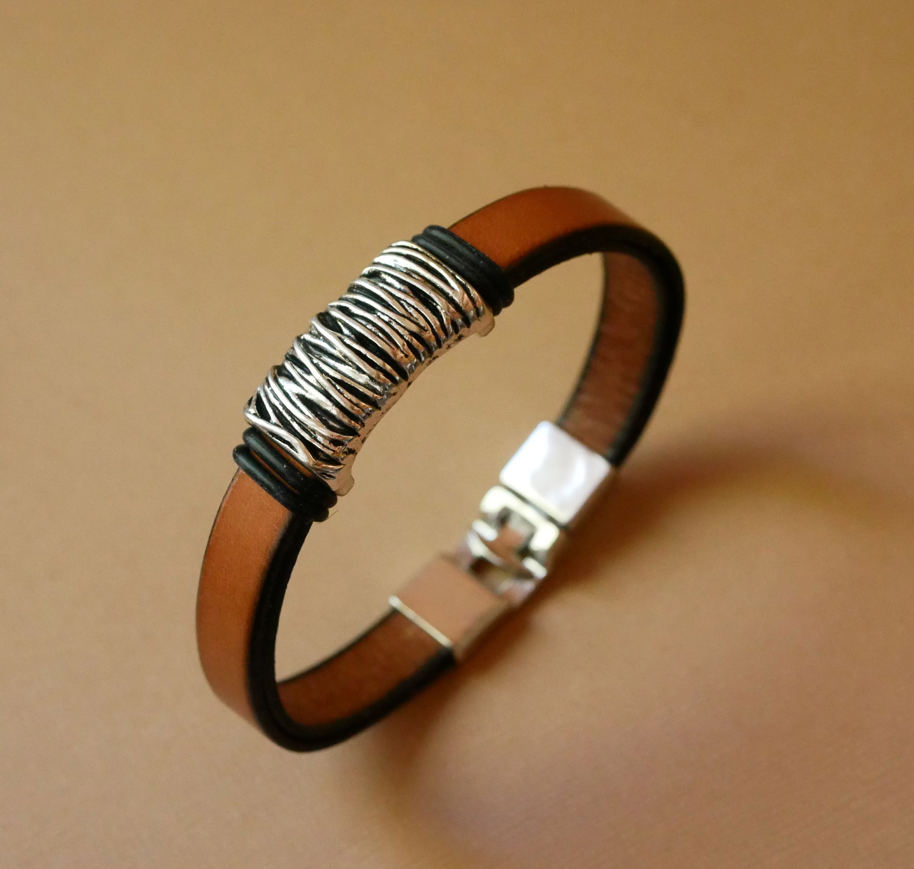 Bracelete em pele camel com decoração em metal entrançado e fecho em forma de T