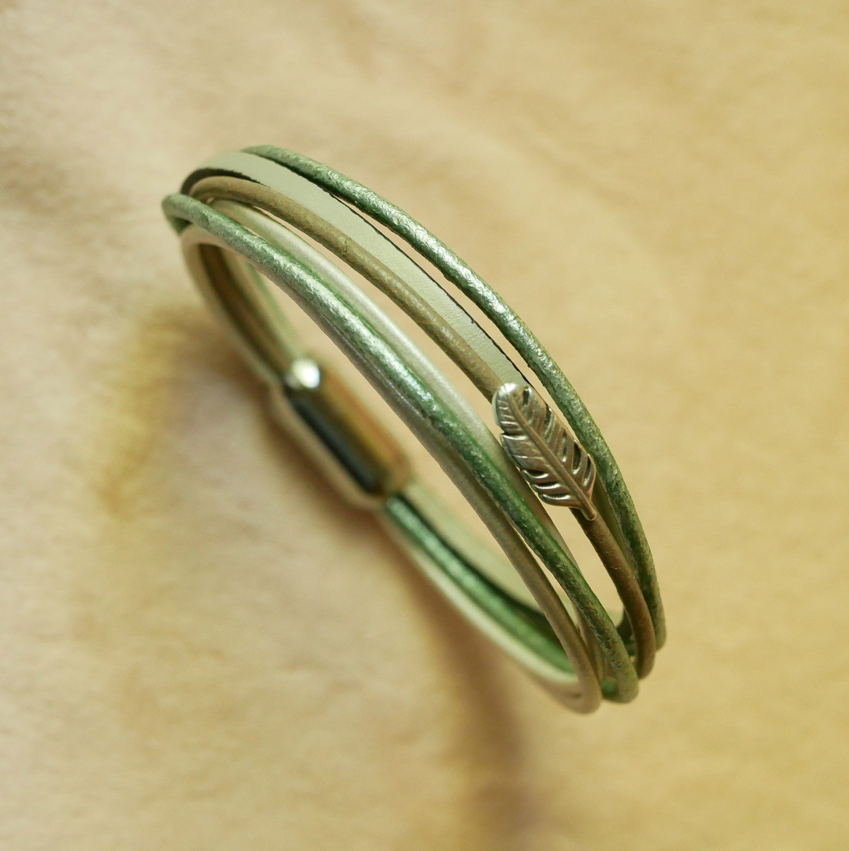 Pulseira multi-couro em tons de bege, verde pálido e perolado, decorada com uma pequena pena