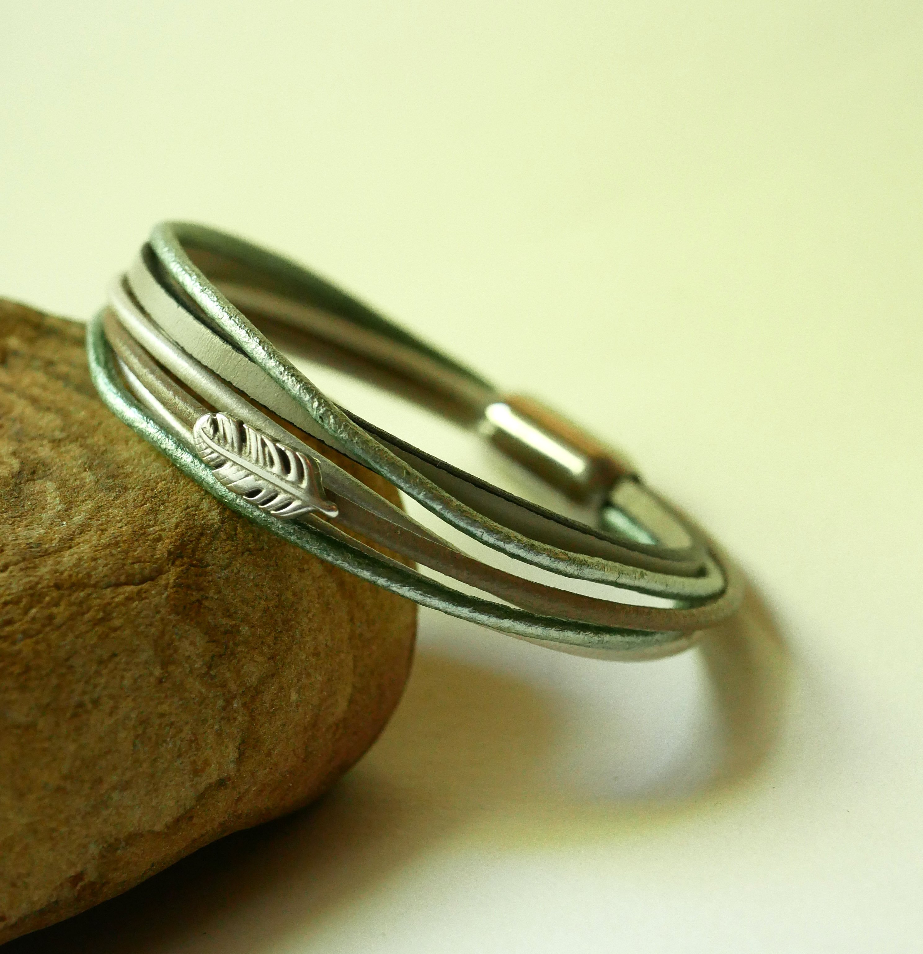 Pulseira multi-couro em tons de bege, verde p&aacute;lido e perolado, decorada com uma pequena pena