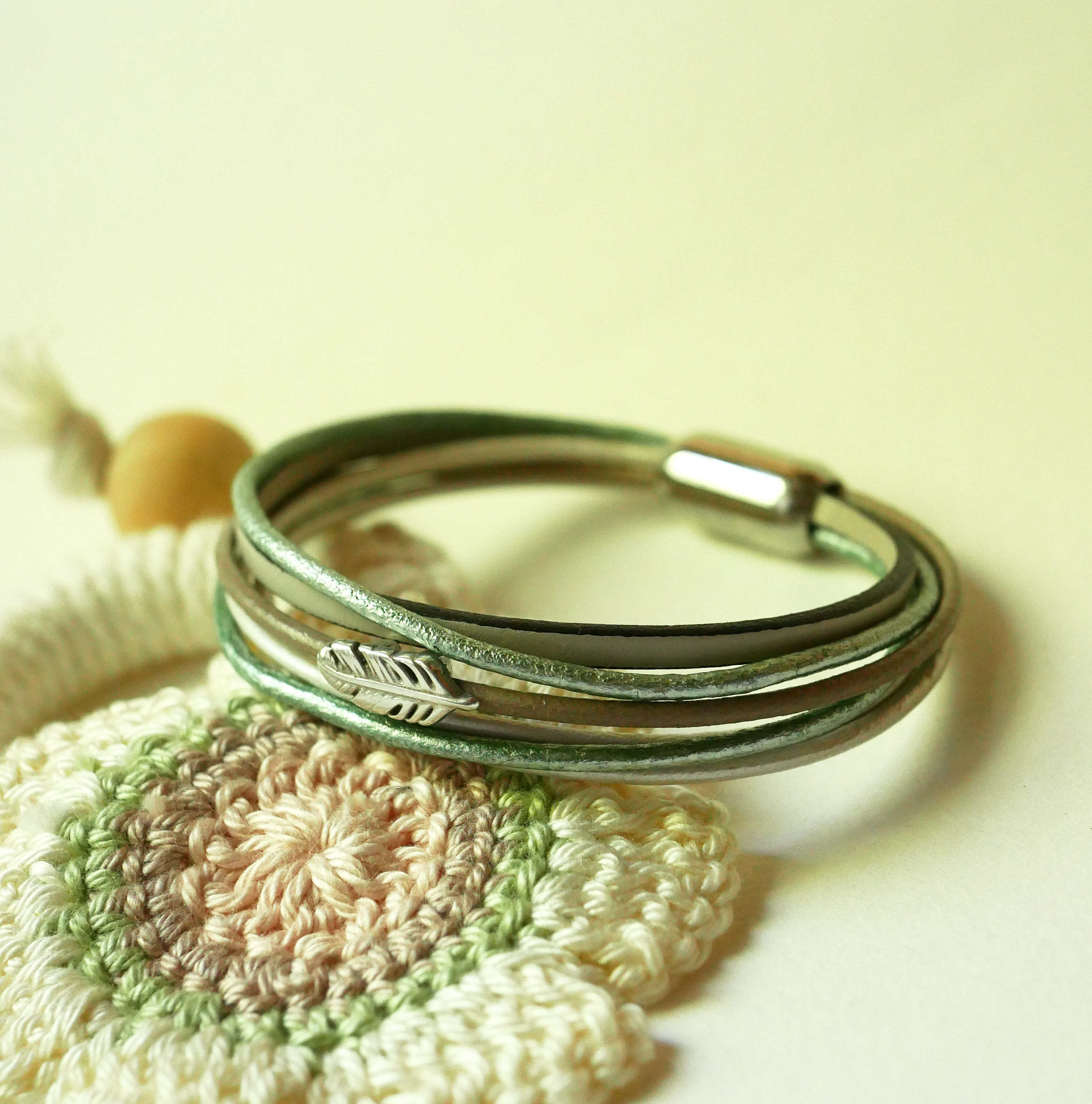 Pulseira multi-couro em tons de bege, verde pálido e perolado, decorada com uma pequena pena
