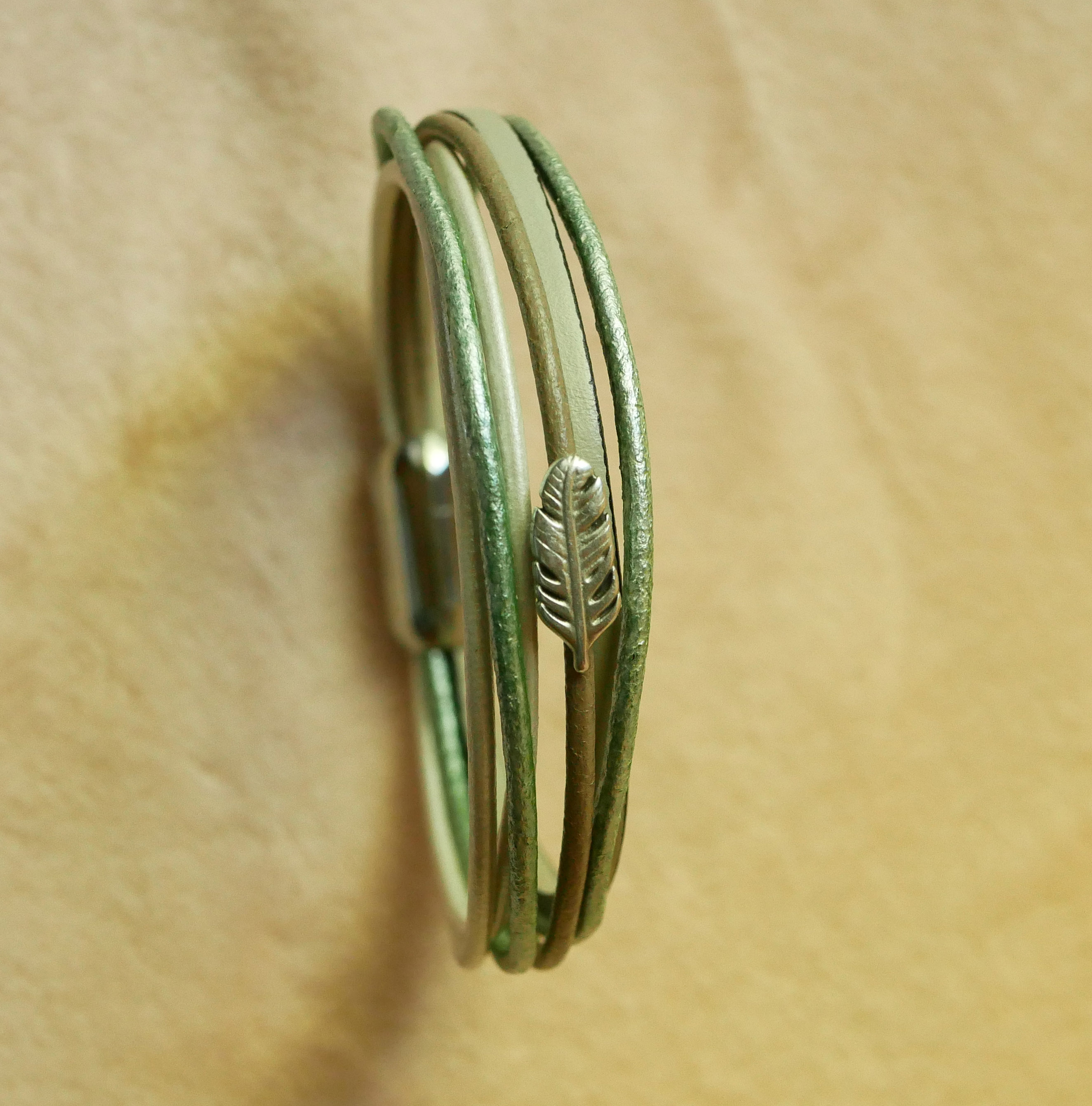 Pulseira multi-couro em tons de bege, verde pálido e perolado, decorada com uma pequena pena