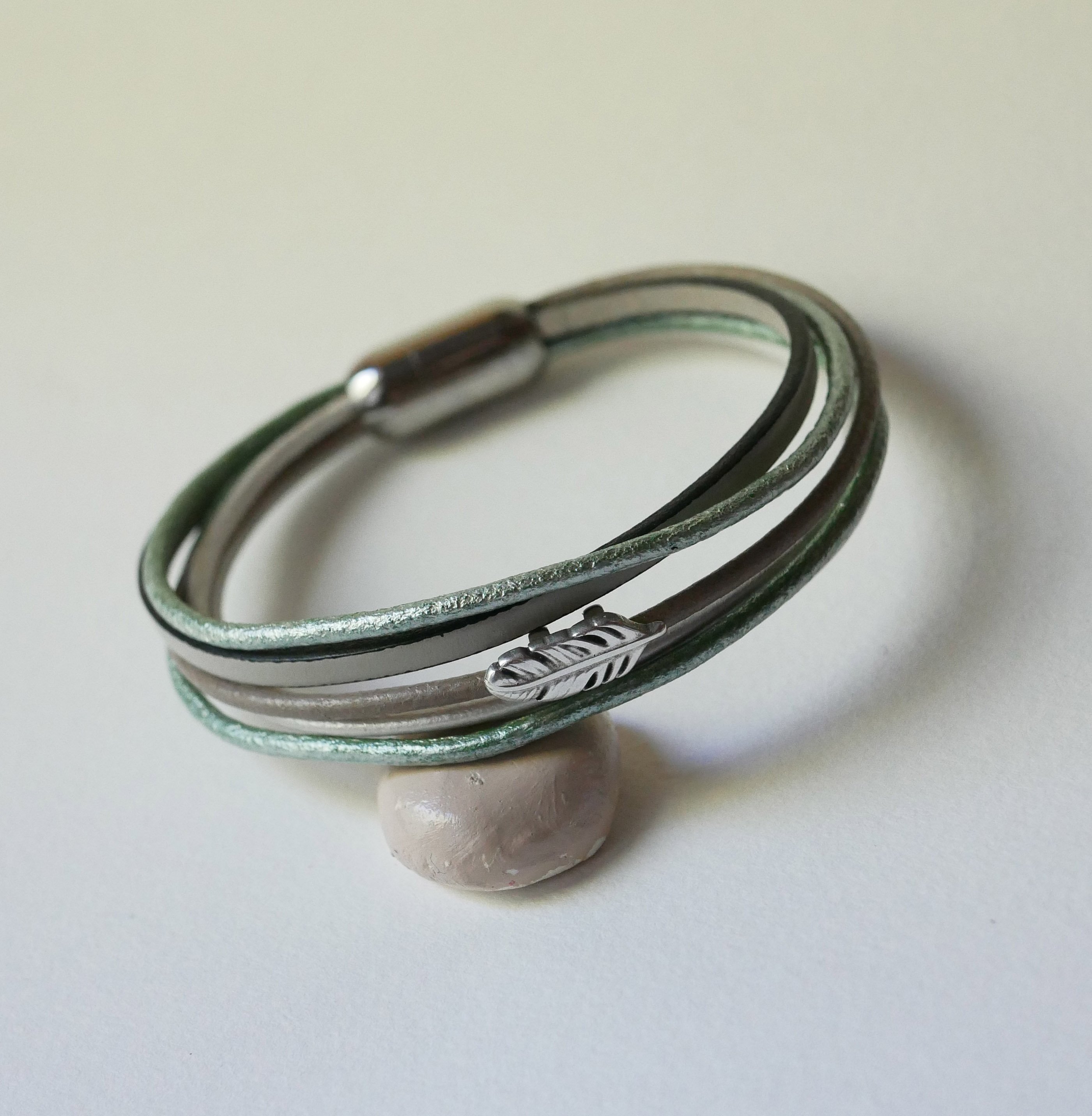 Pulseira multi-couro em tons de bege, verde pálido e perolado, decorada com uma pequena pena