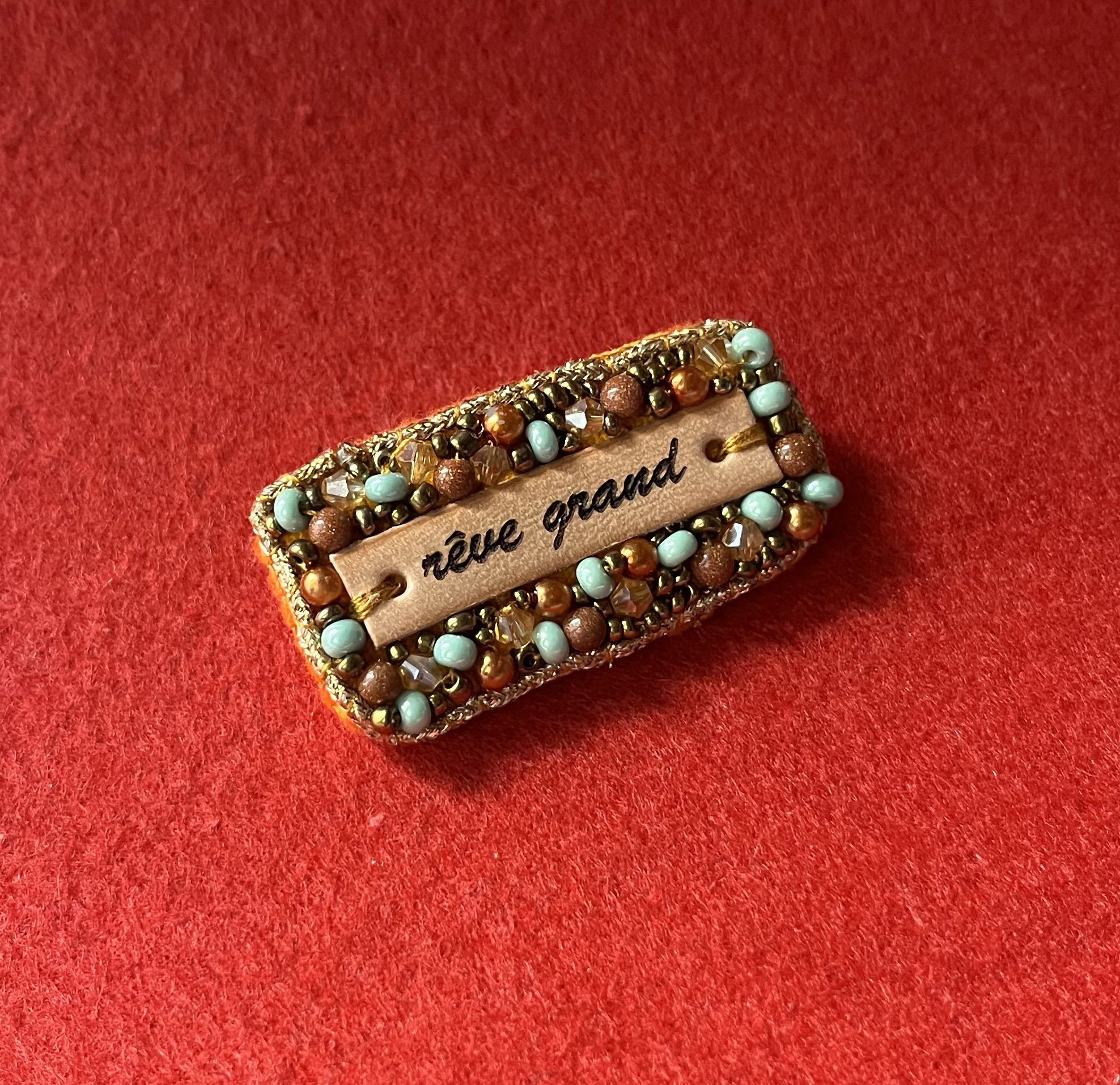 Broche en perles dor&eacute;es &agrave; message en cuir grav&eacute; "r&ecirc;ve grand"