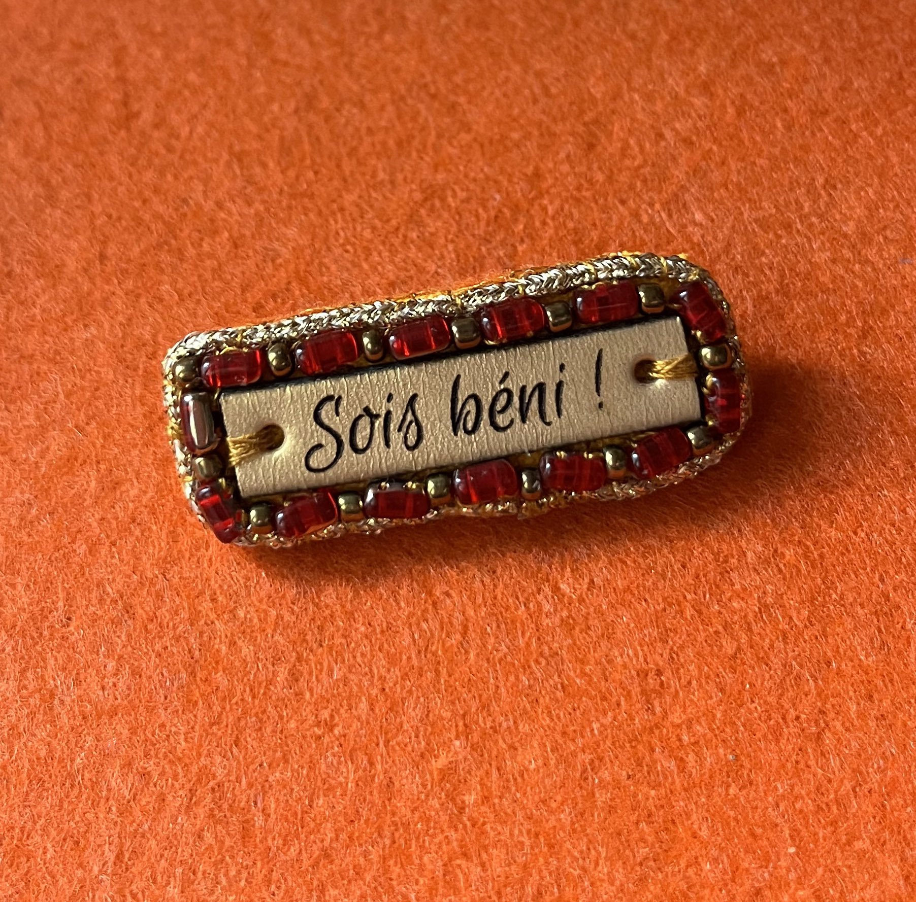 Broche &agrave; message en cuir grav&eacute; "sois b&eacute;ni" en perles rouges et dor&eacute;es 