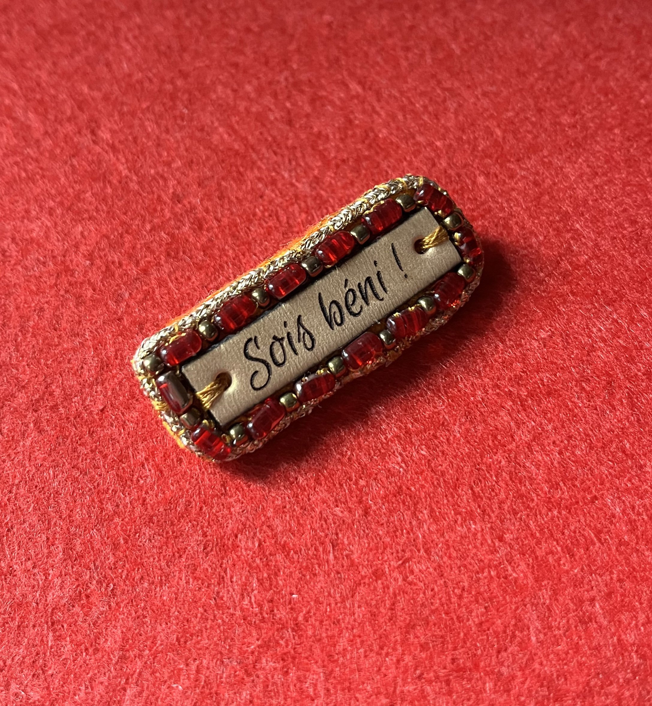 Broche &agrave; message en cuir grav&eacute; "sois b&eacute;ni" en perles rouges et dor&eacute;es 