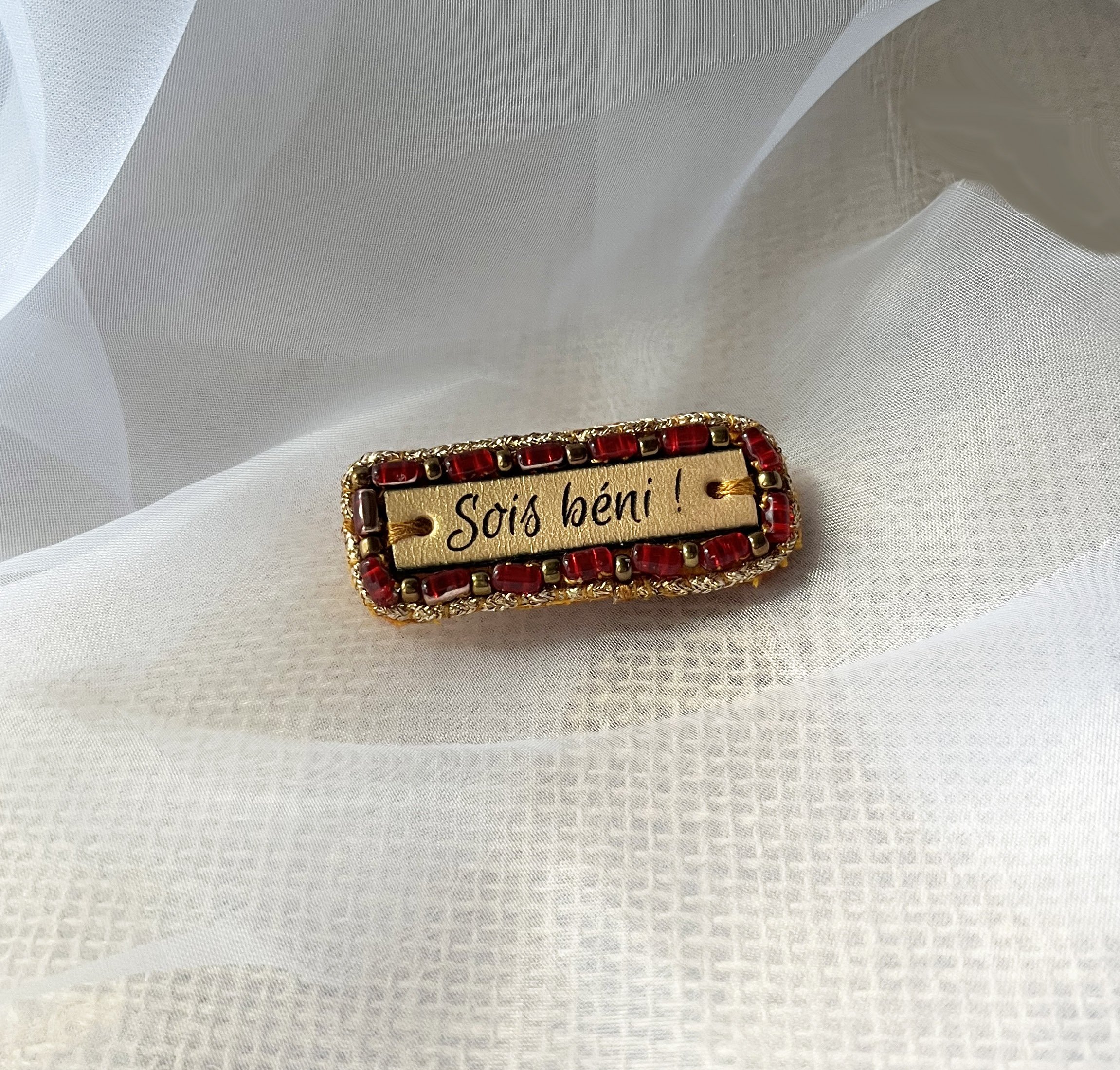 Broche &agrave; message en cuir grav&eacute; "sois b&eacute;ni" en perles rouges et dor&eacute;es 