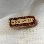 Broche &agrave; message en cuir grav&eacute; "sois b&eacute;ni" en perles rouges et dor&eacute;es 